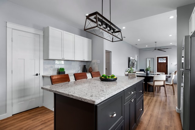 kitchen with a kitchen island, light wood-type flooring, hanging light fixtures, white cabinets, and ceiling fan