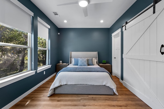 bedroom with hardwood / wood-style flooring, a barn door, and ceiling fan