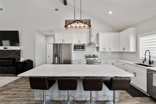 kitchen with wall chimney exhaust hood, a kitchen island, sink, and appliances with stainless steel finishes