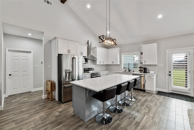 kitchen featuring white cabinetry, a kitchen island, stainless steel appliances, and wall chimney range hood