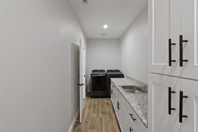 kitchen with white cabinets, washing machine and dryer, light stone countertops, and sink