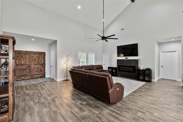 living room featuring hardwood / wood-style floors, ceiling fan, a stone fireplace, and high vaulted ceiling