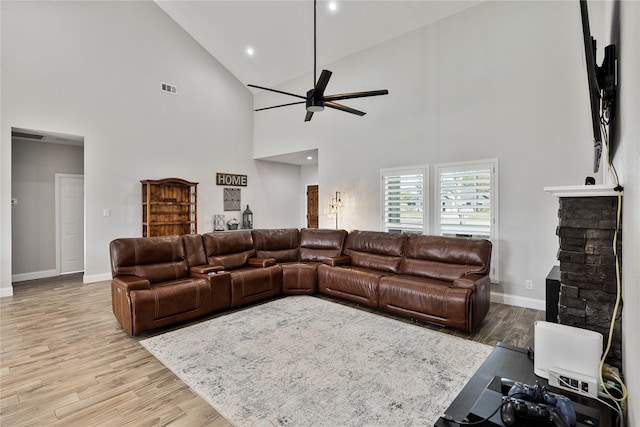 living room featuring light hardwood / wood-style flooring, high vaulted ceiling, ceiling fan, and a stone fireplace