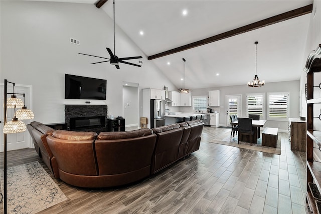 living room with a fireplace, beamed ceiling, ceiling fan with notable chandelier, and high vaulted ceiling