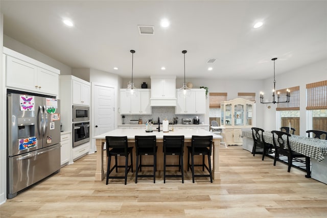 kitchen with stainless steel appliances, white cabinetry, a large island with sink, and decorative light fixtures