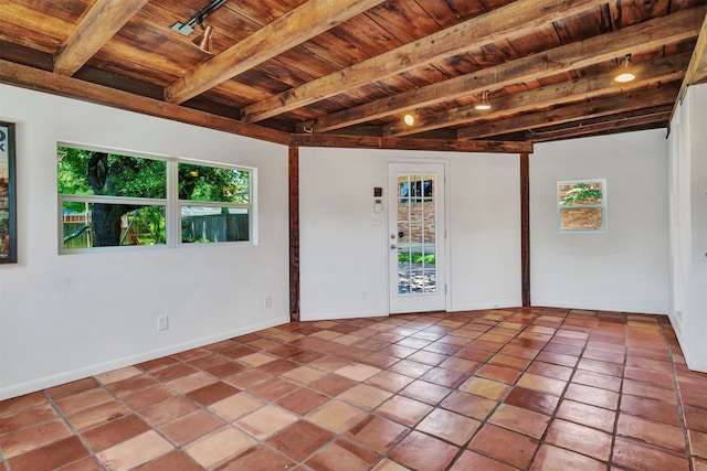 empty room featuring beamed ceiling, a healthy amount of sunlight, tile patterned floors, and wood ceiling