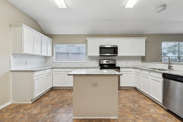 kitchen with white cabinetry, light stone countertops, sink, stainless steel appliances, and vaulted ceiling