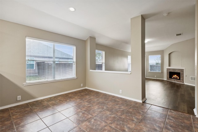 unfurnished room with a tiled fireplace, a wealth of natural light, and dark tile patterned floors