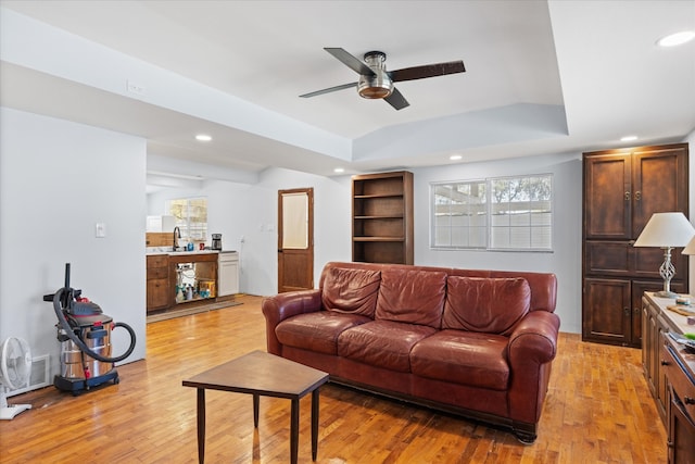 living room featuring light wood-type flooring, sink, ceiling fan, and a tray ceiling