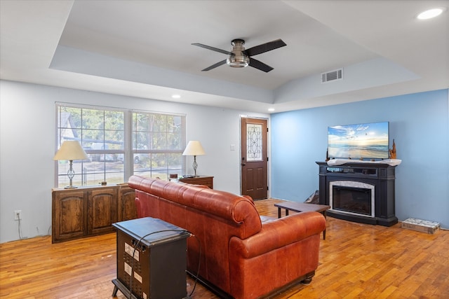 living room with ceiling fan, a tray ceiling, and light hardwood / wood-style floors