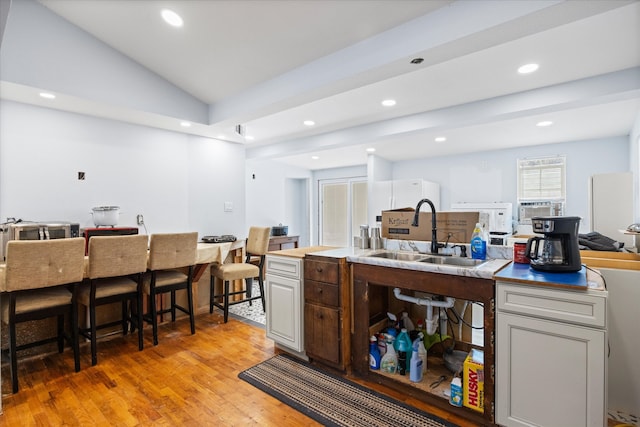 kitchen with sink, vaulted ceiling, and light hardwood / wood-style floors