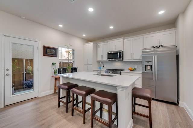 kitchen featuring stainless steel appliances, a center island with sink, white cabinets, sink, and a breakfast bar area