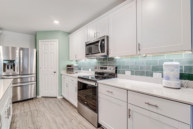 kitchen with stainless steel appliances, light stone counters, backsplash, light hardwood / wood-style floors, and white cabinets