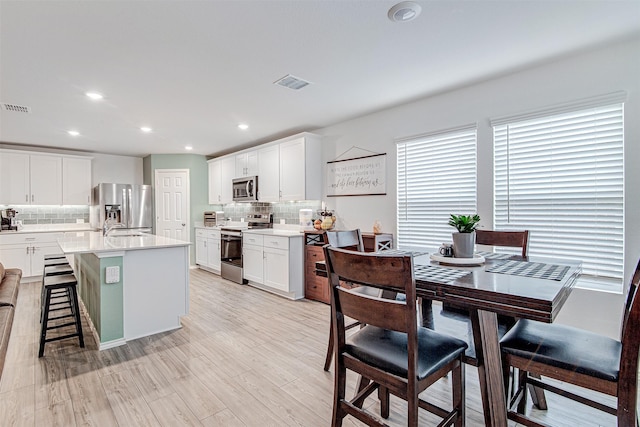 kitchen with backsplash, a kitchen island with sink, appliances with stainless steel finishes, a kitchen bar, and white cabinetry