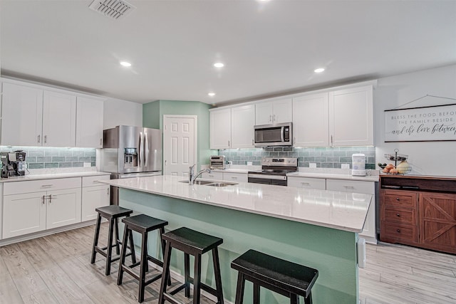 kitchen featuring white cabinets, a breakfast bar, a kitchen island with sink, and appliances with stainless steel finishes