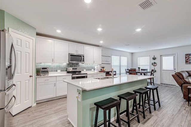 kitchen featuring a kitchen breakfast bar, stainless steel appliances, sink, white cabinets, and an island with sink