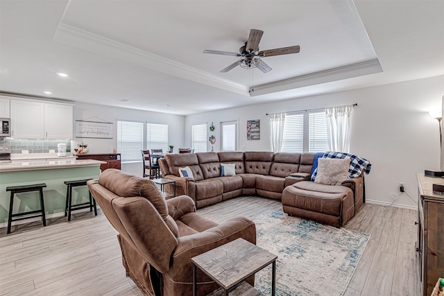 living room featuring a tray ceiling, ceiling fan, and light wood-type flooring