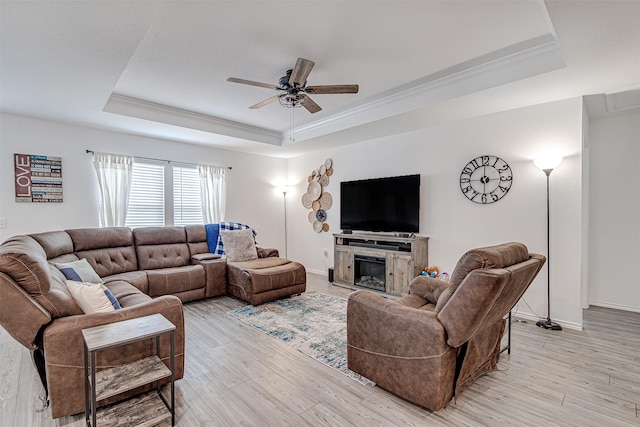 living room featuring ceiling fan, ornamental molding, light hardwood / wood-style flooring, and a tray ceiling