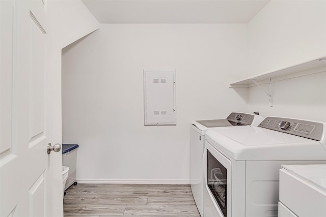 laundry area with electric panel, washing machine and dryer, light hardwood / wood-style floors, and sink