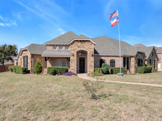 french provincial home featuring brick siding, roof with shingles, metal roof, fence, and a front lawn