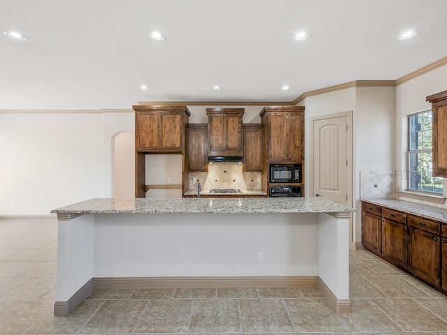 kitchen featuring black appliances, light stone countertops, crown molding, a large island, and decorative backsplash