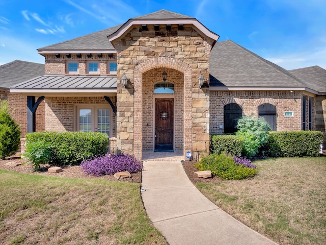 view of front of property with brick siding, a shingled roof, a front yard, a standing seam roof, and stone siding