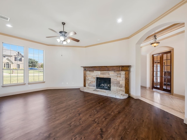 unfurnished living room featuring hardwood / wood-style flooring, ceiling fan, a stone fireplace, crown molding, and french doors