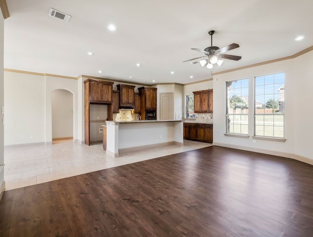 kitchen with black microwave, ornamental molding, a spacious island, and light hardwood / wood-style flooring