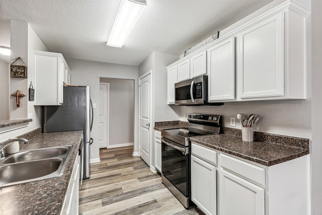 kitchen with stainless steel appliances, a textured ceiling, sink, white cabinetry, and light hardwood / wood-style flooring