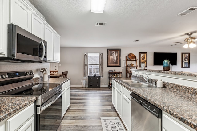 kitchen featuring sink, appliances with stainless steel finishes, a textured ceiling, wood-type flooring, and white cabinets