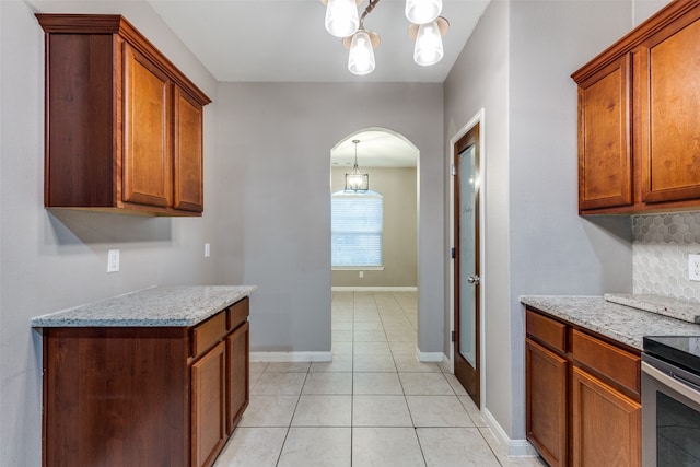 kitchen featuring light stone counters, electric stove, a chandelier, tasteful backsplash, and light tile patterned floors