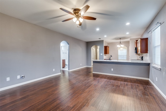 unfurnished living room with ceiling fan with notable chandelier, dark wood-type flooring, and sink