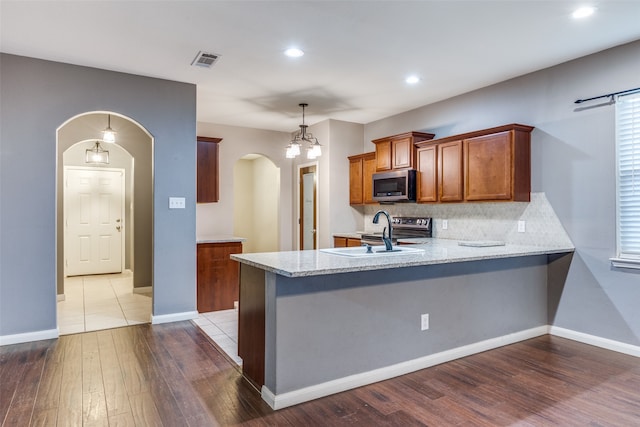 kitchen featuring stainless steel appliances, hardwood / wood-style floors, kitchen peninsula, sink, and decorative light fixtures