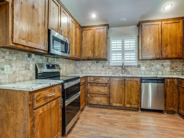 kitchen with sink, appliances with stainless steel finishes, backsplash, light stone counters, and light wood-type flooring