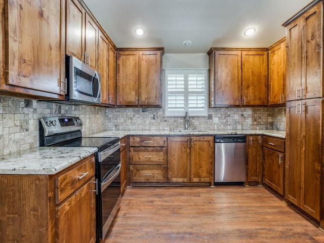 kitchen with sink, decorative backsplash, light hardwood / wood-style floors, light stone counters, and stainless steel appliances