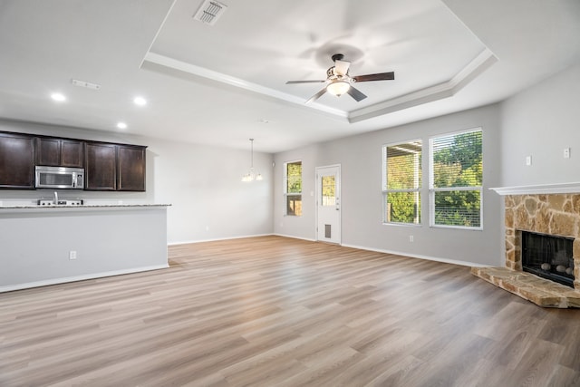 unfurnished living room with ceiling fan with notable chandelier, a raised ceiling, and light wood-type flooring