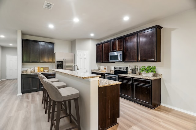 kitchen with a kitchen breakfast bar, light hardwood / wood-style floors, a kitchen island with sink, and appliances with stainless steel finishes