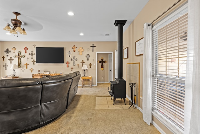 living room with a wood stove, light carpet, and ceiling fan