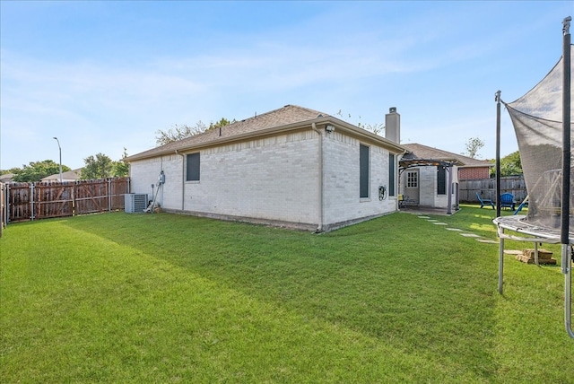 rear view of property featuring central AC, a yard, and a trampoline