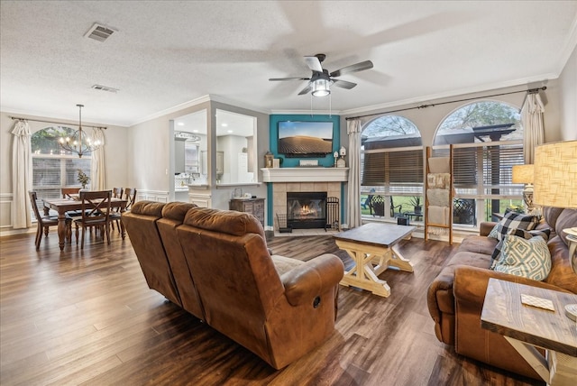 living room featuring ceiling fan with notable chandelier, ornamental molding, a textured ceiling, dark hardwood / wood-style flooring, and a tiled fireplace