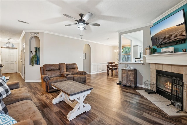 living room with ceiling fan, ornamental molding, a textured ceiling, wood-type flooring, and a tiled fireplace