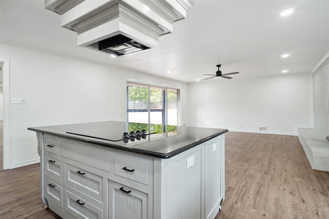 kitchen featuring cooktop, ceiling fan, crown molding, a center island, and light wood-type flooring