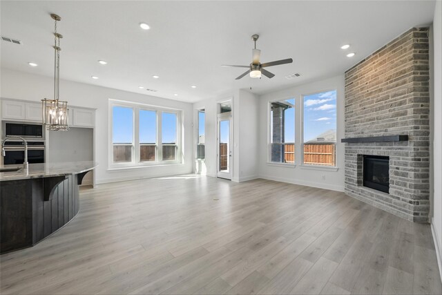 unfurnished living room with visible vents, light wood-type flooring, ceiling fan with notable chandelier, and a large fireplace