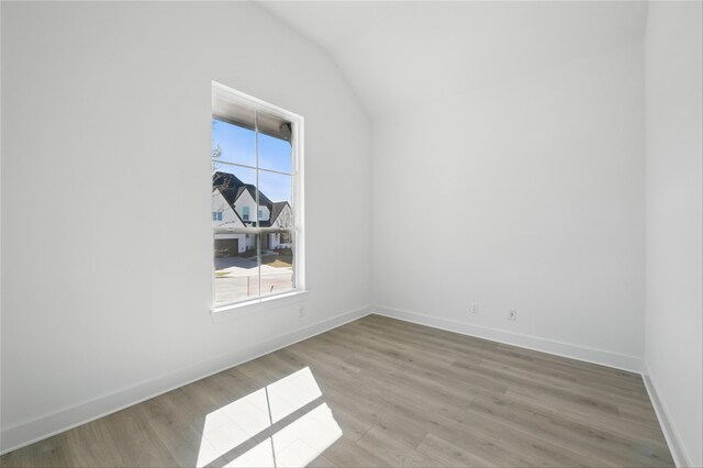 empty room featuring a wealth of natural light, light wood finished floors, vaulted ceiling, and baseboards