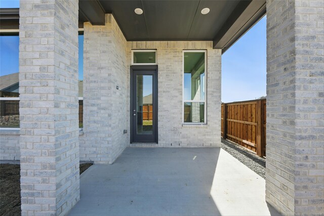 entrance to property featuring a patio area, brick siding, and fence