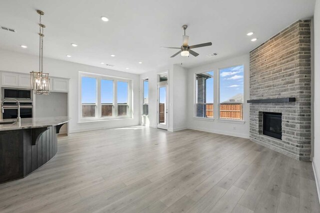 unfurnished living room with visible vents, ceiling fan with notable chandelier, light wood finished floors, and a fireplace