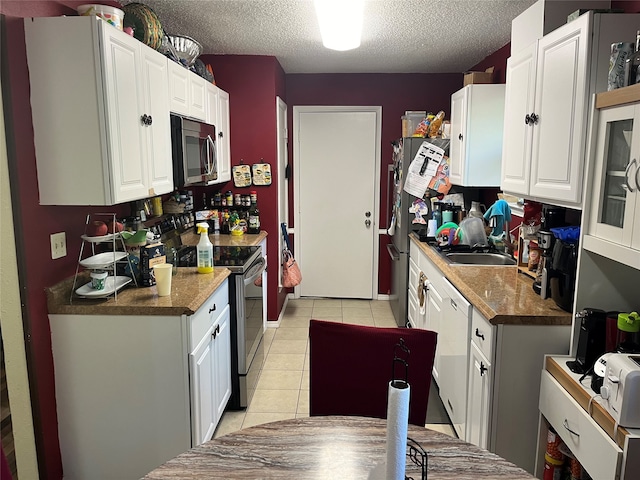 kitchen featuring sink, appliances with stainless steel finishes, a textured ceiling, light tile patterned floors, and white cabinets