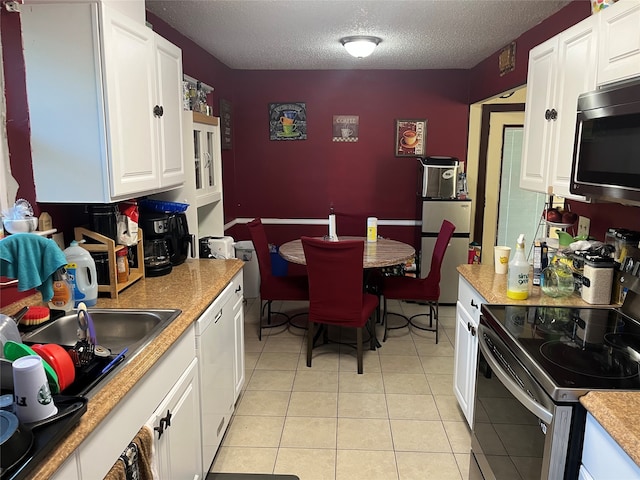 kitchen featuring sink, appliances with stainless steel finishes, a textured ceiling, light tile patterned floors, and white cabinets