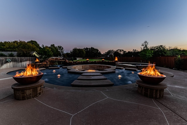 pool at dusk featuring an outdoor fire pit, a patio, and an in ground hot tub