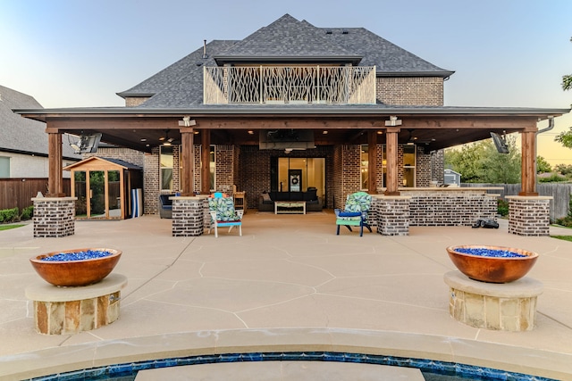 rear view of property with a balcony, ceiling fan, an outdoor living space with a fire pit, and a patio area